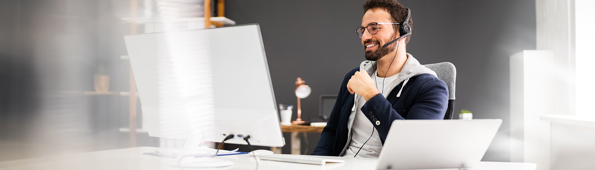 Mann in weißem Büro vor Laptop mit Headset