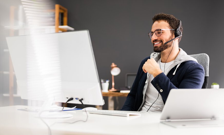 Mann in weißem Büro vor Laptop mit Headset