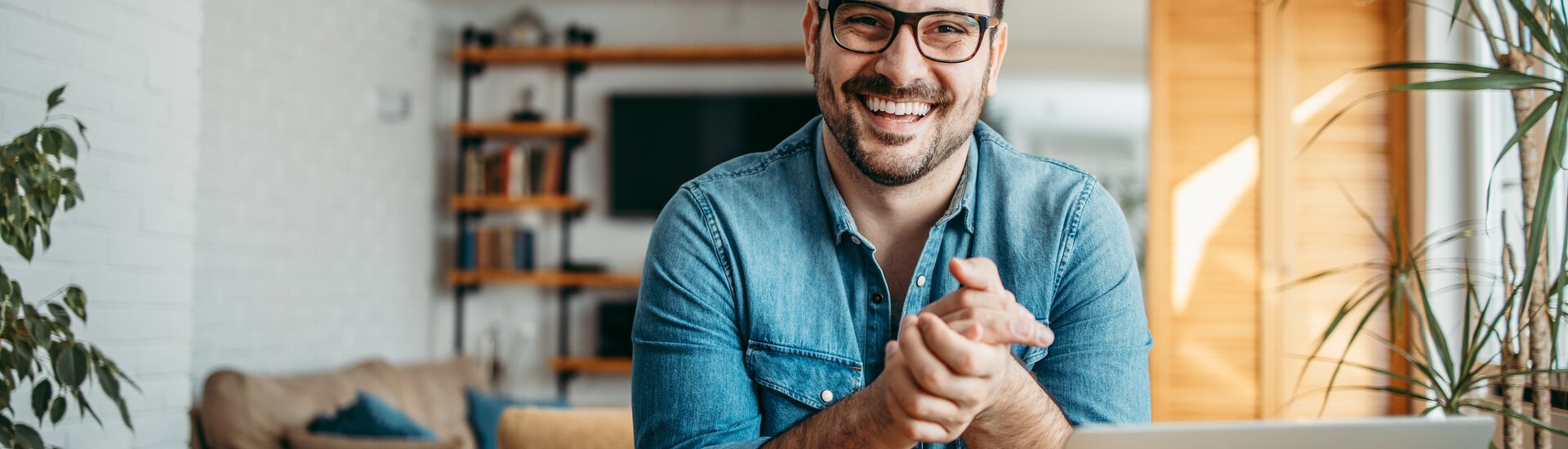 Positive gestimmter Mann sitzt vor geöffnetem Laptop an Schreibtisch