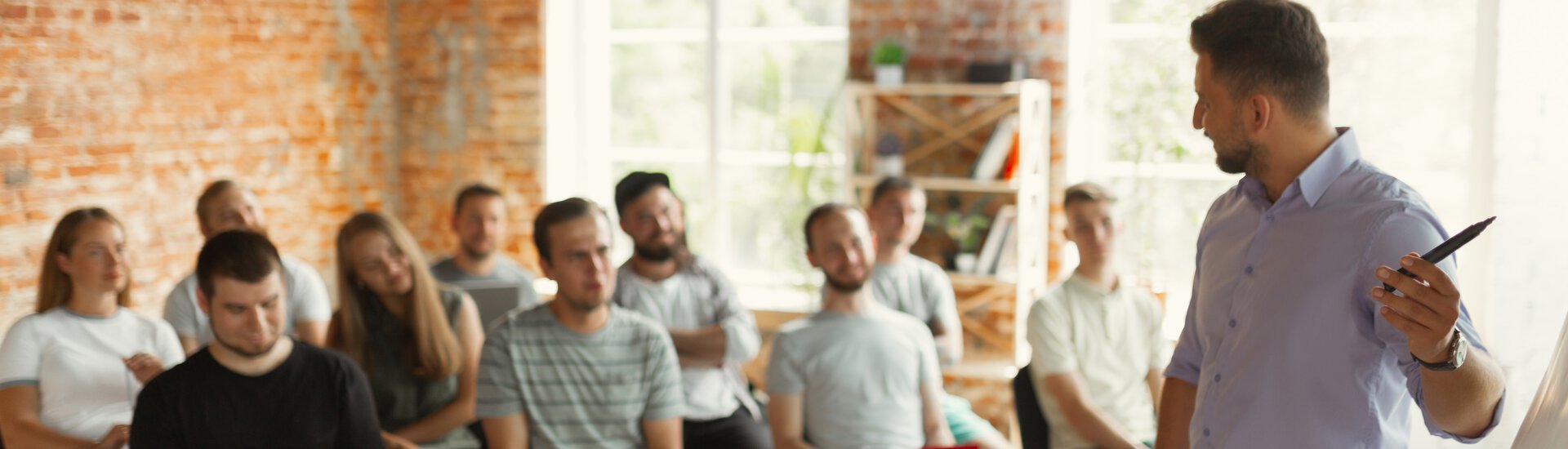 Mann unterrichtet stehend vor Klasse mittleren Alters und zeigt auf ein Whiteboard