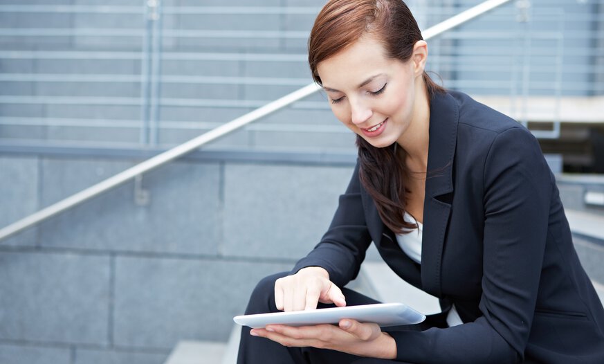 Frau sitzt draußen auf Treppen mit einem Tablet in der Handy