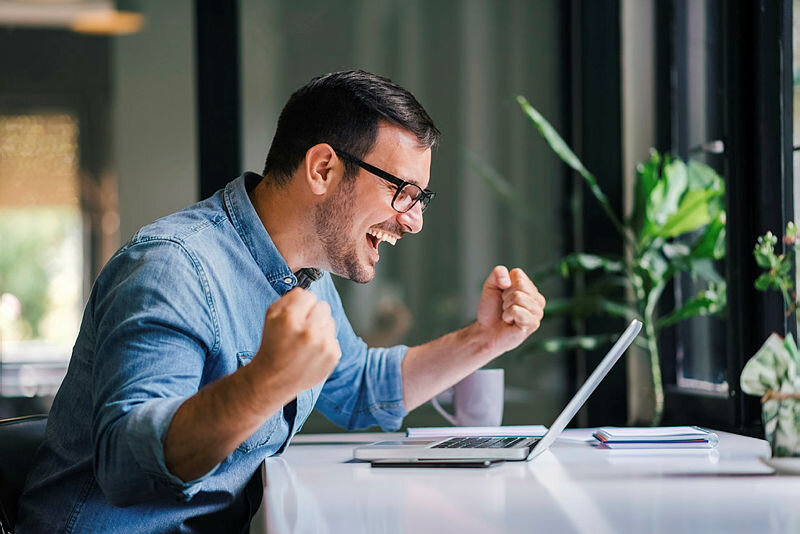 Junger Mann mit Brille freut sich vor Laptop