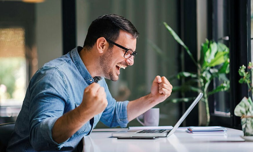 Junger Mann mit Brille freut sich vor Laptop