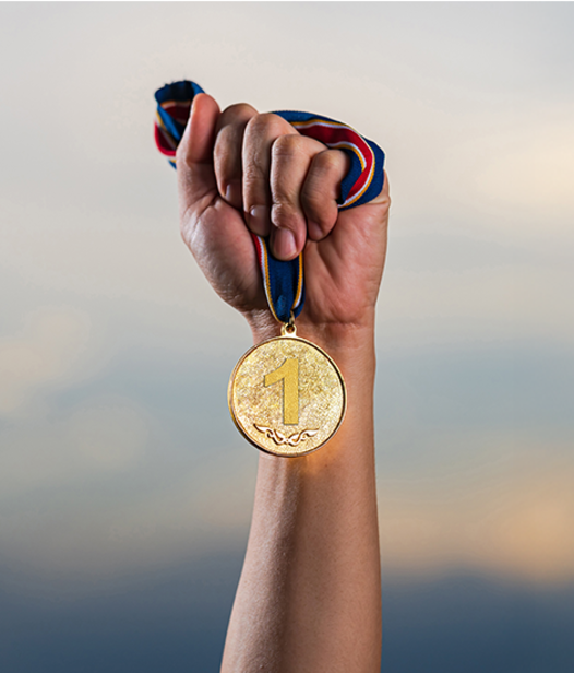 Arm getreckt nach oben und hält goldene Medaille in der Hand