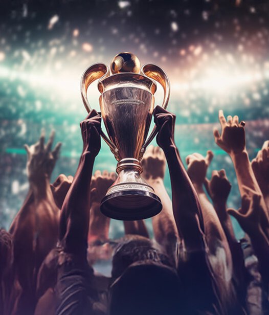 Großer goldener Pokal wird von jubelnder Menge in einem Stadium in die Höhe gehalten. 