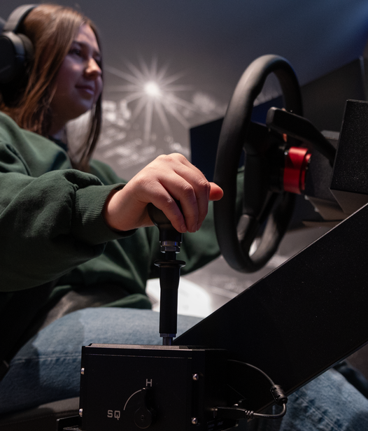 Fahrschülerin sitzt gut gelaunt an Simulator Premium und schaltet