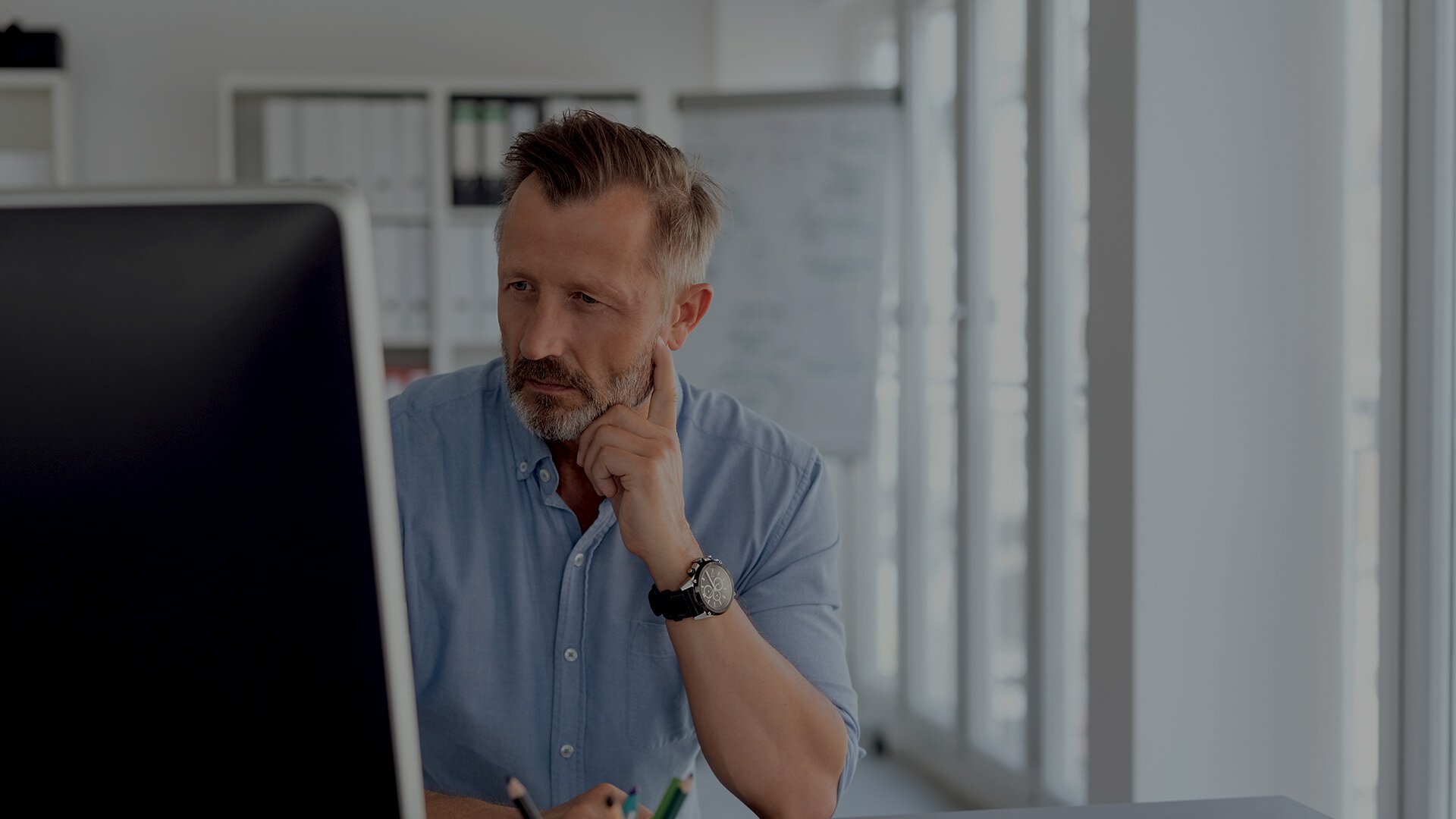 Mann mit blauem Hemd in Büro sitzt hinter einem Computer Bildschirm