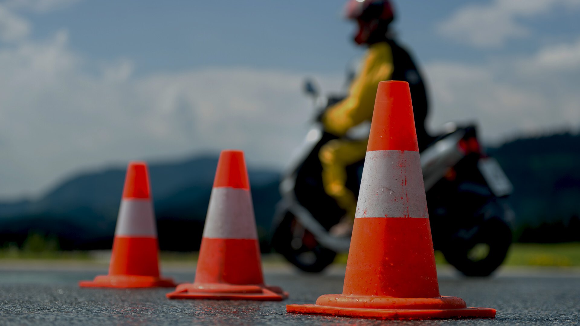 Drei orange Leitkegel mit fahrendem Roller im Hintergrund