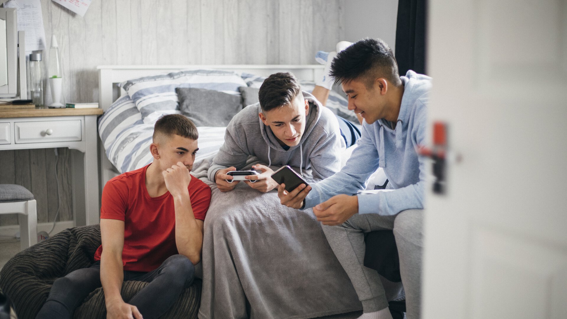 Drei männliche Teenager haben ein Handy in der Hand und zeigen sich was